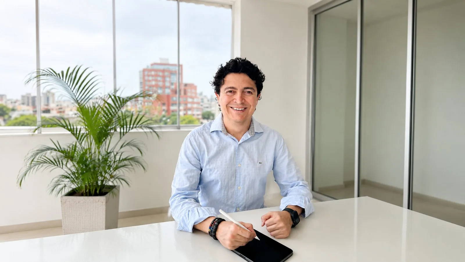 César Torres, sonriendo, sentado a la mesa de su oficina mientras escribe en una tableta con un lápiz digital.